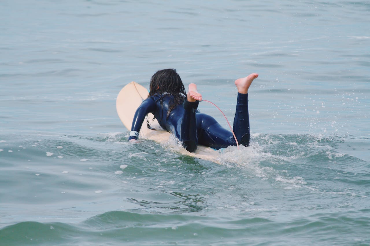 A child on a surfboard paddling through ocean waves during a sunny summer day.