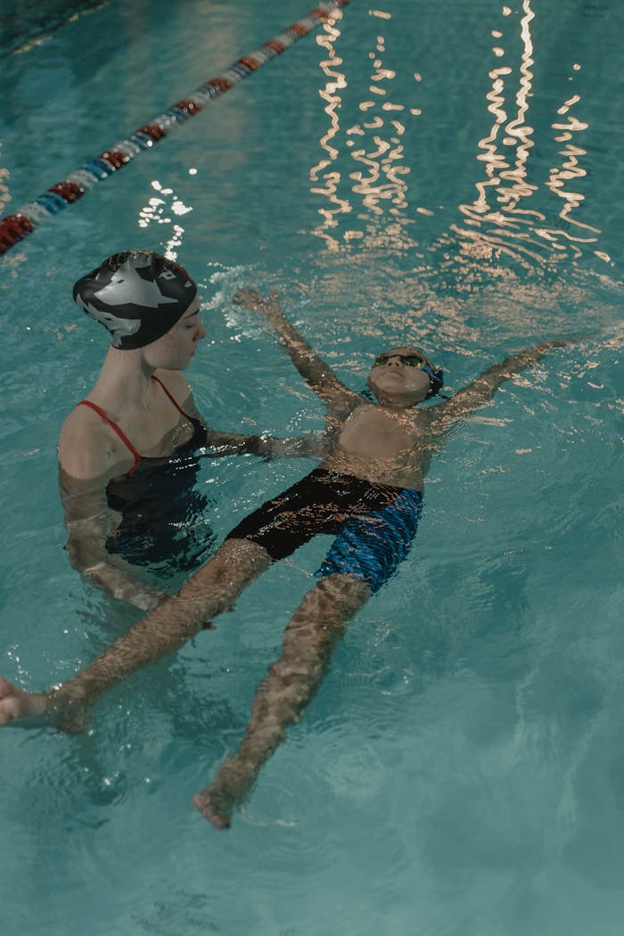 A child learning to swim with the guidance of an instructor in an indoor swimming pool.