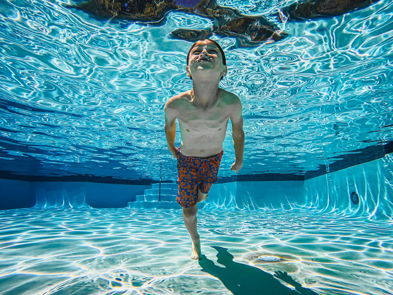 A joyful child swims underwater in a sunlit swimming pool, showcasing fun and skill.